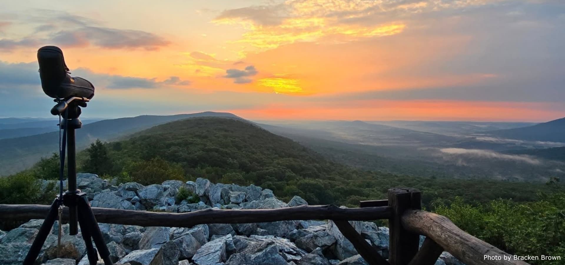 A telescope overlooks a scenic mountain landscape at sunrise.