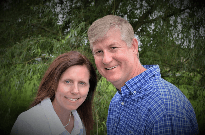 A couple poses together in front of a green background, smiling at the camera.