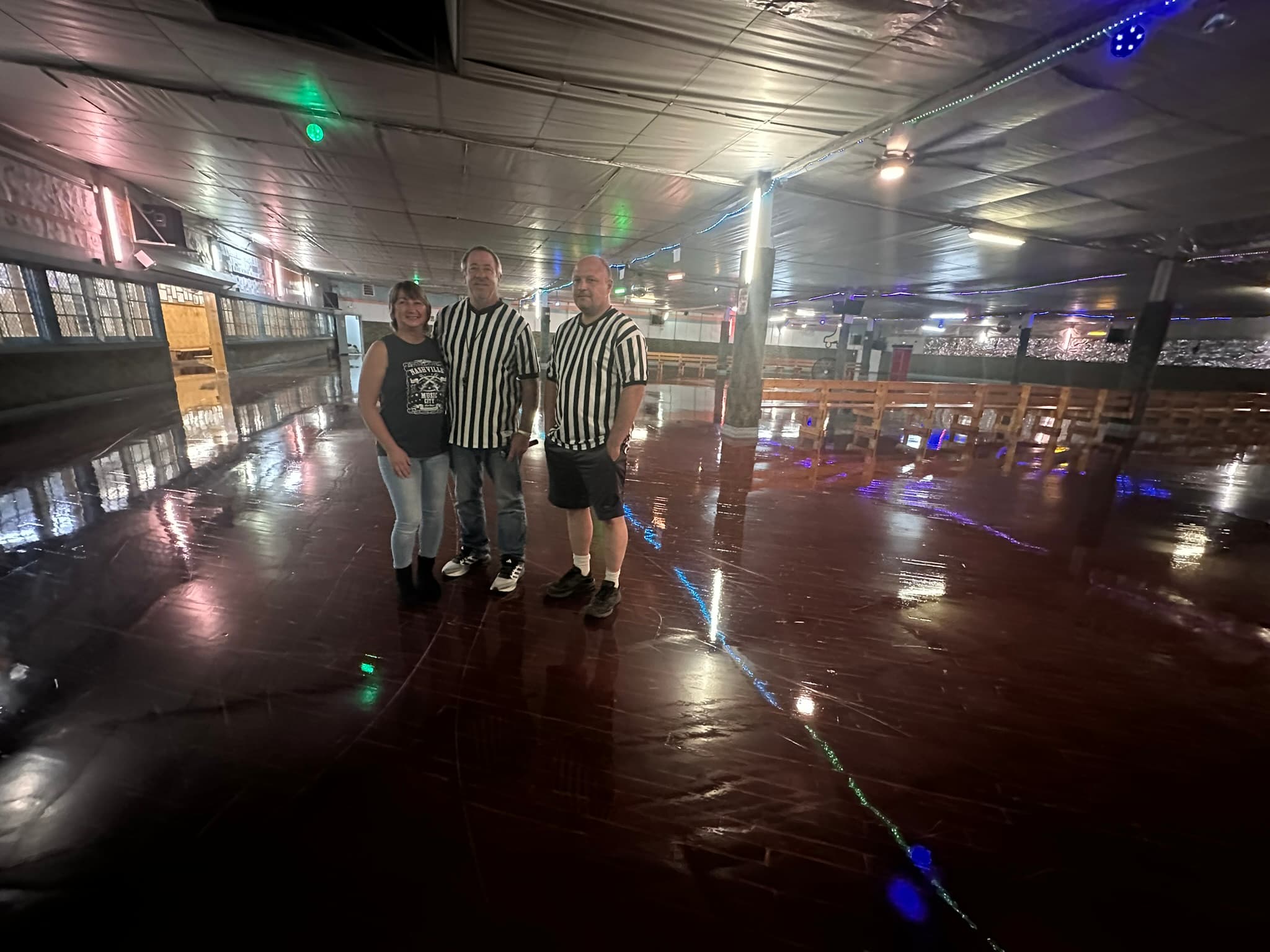 Three individuals in black and white striped shirts pose in a spacious, dimly lit venue with a shiny floor.