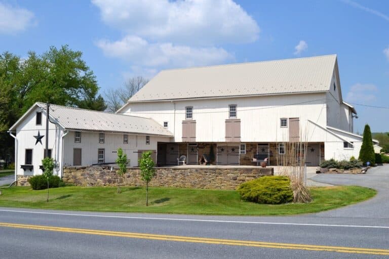 A large white barn with a metal roof and an adjacent smaller building, set against a clear blue sky.
