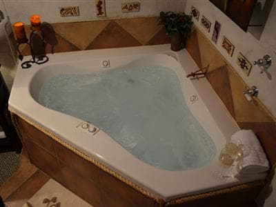 A spacious, triangular hot tub filled with water, surrounded by candles and decorative tiles.