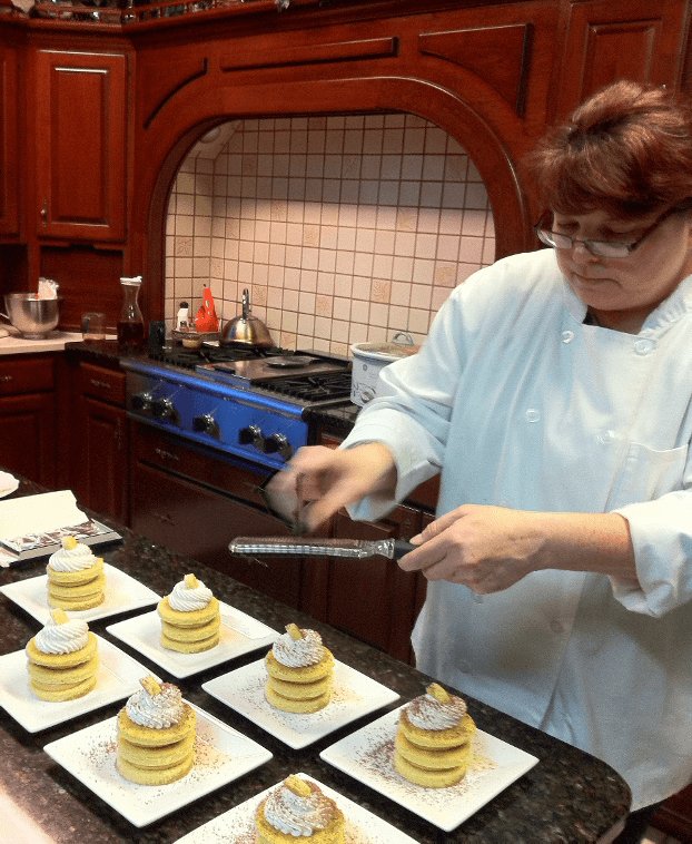 A chef decorates layered desserts in a warm kitchen.