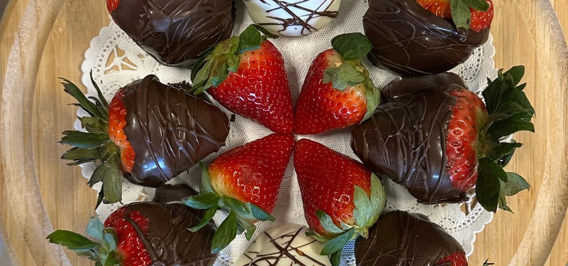A wooden platter filled with chocolate-covered strawberries arranged in a decorative pattern.