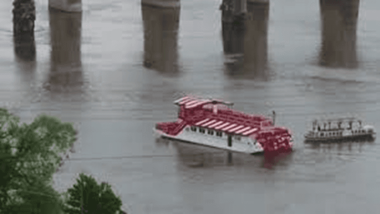 Two boats navigate a flooded river beneath a bridge.