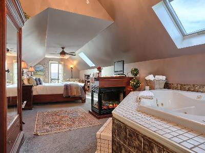 Cozy attic bedroom featuring a fireplace, a jetted tub, and a skylight.