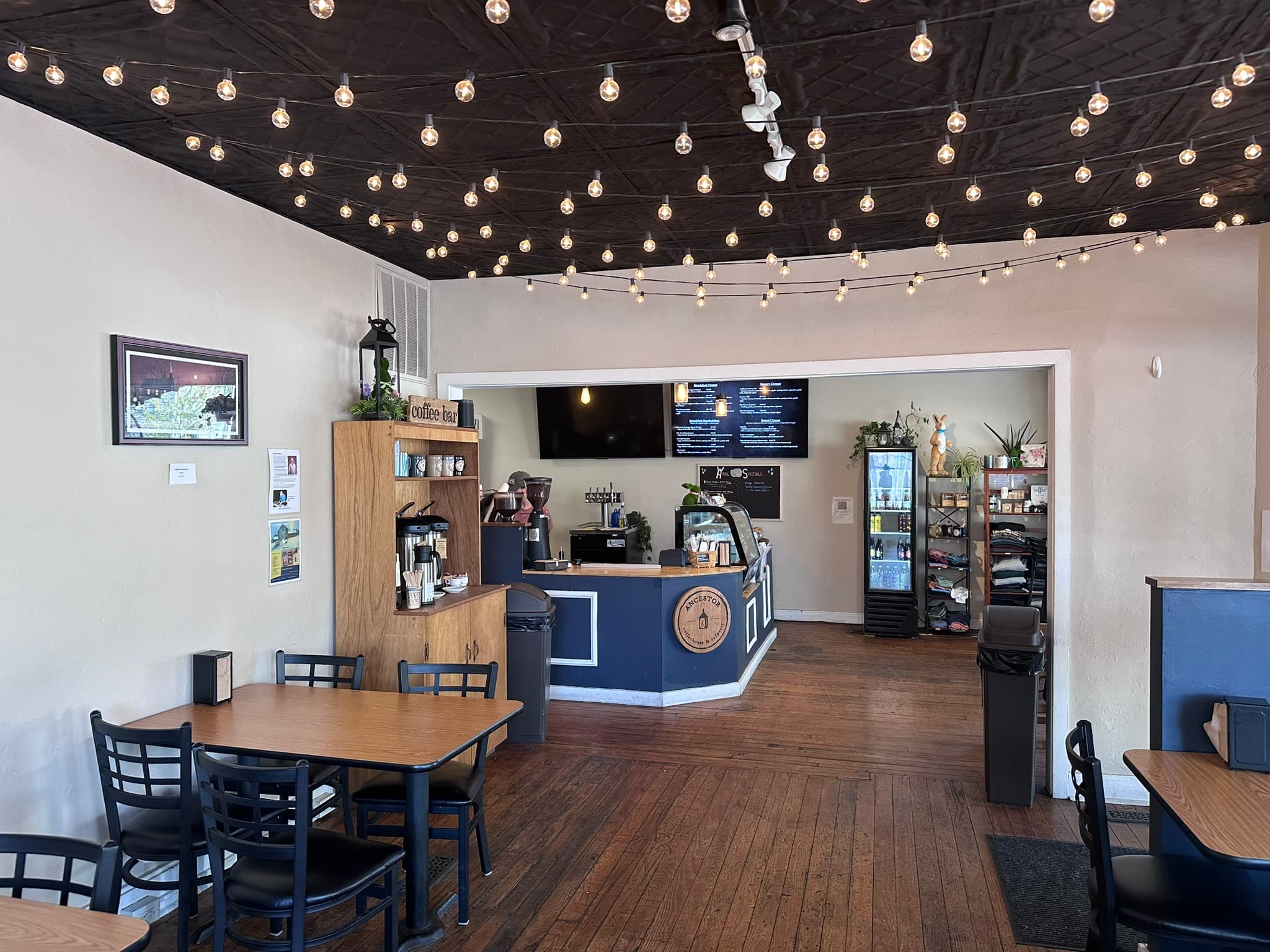 Cozy café interior featuring wooden tables, a service counter, and string lights overhead.