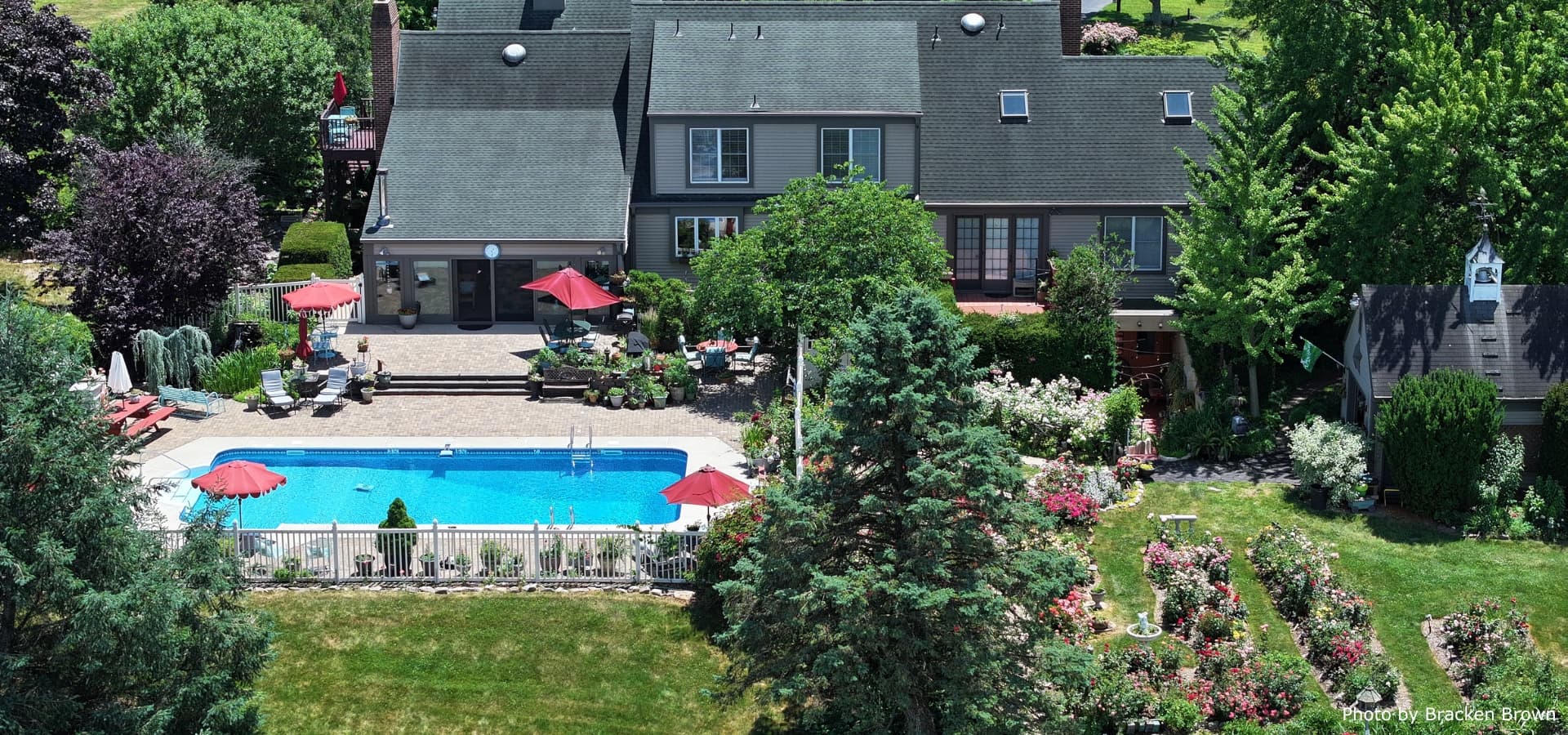 Aerial view of a spacious backyard featuring a swimming pool, patio furniture, and a variety of lush plants and flowers.