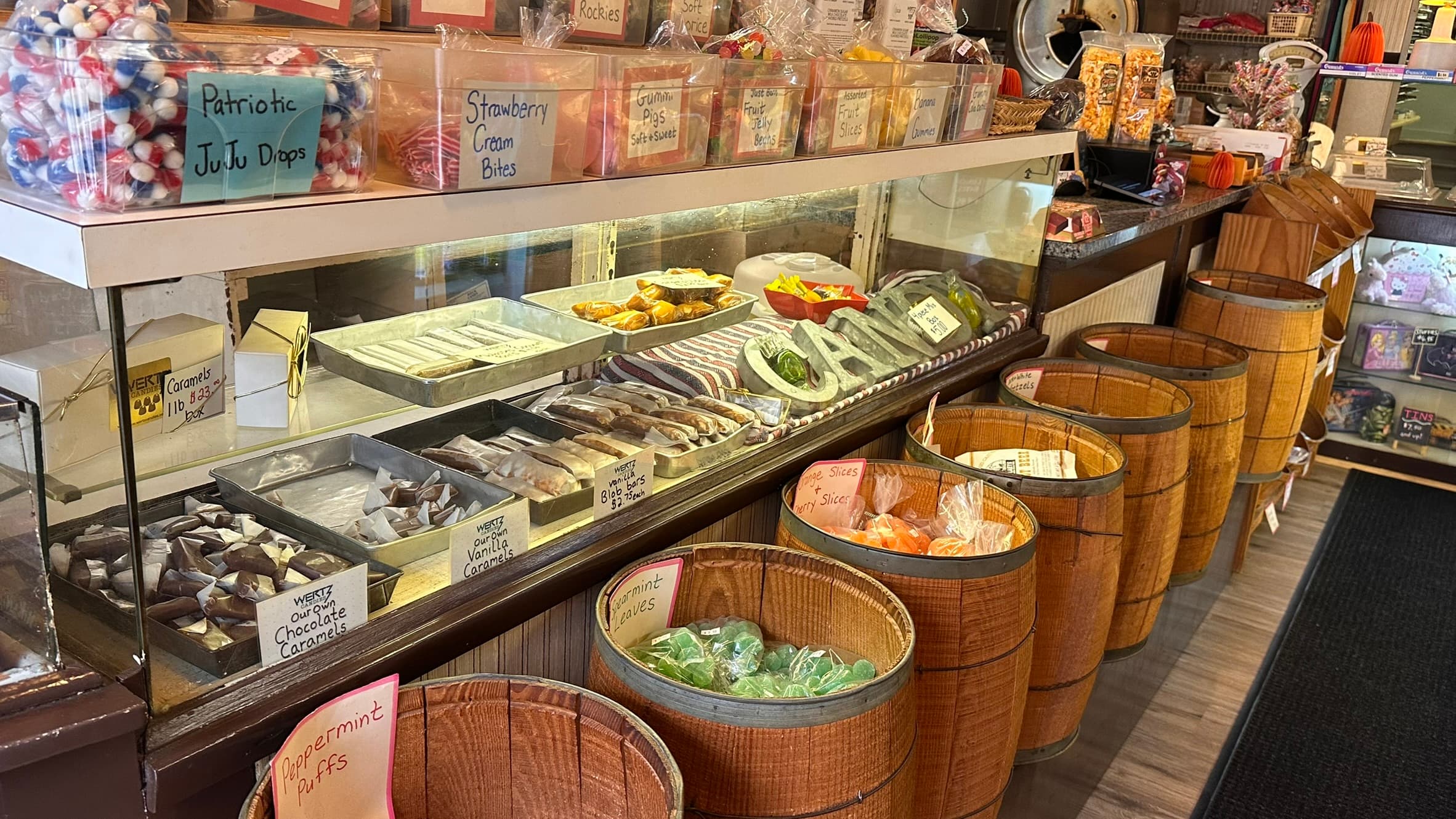 A glass display case filled with assorted candies, surrounded by wooden barrels of various confections.