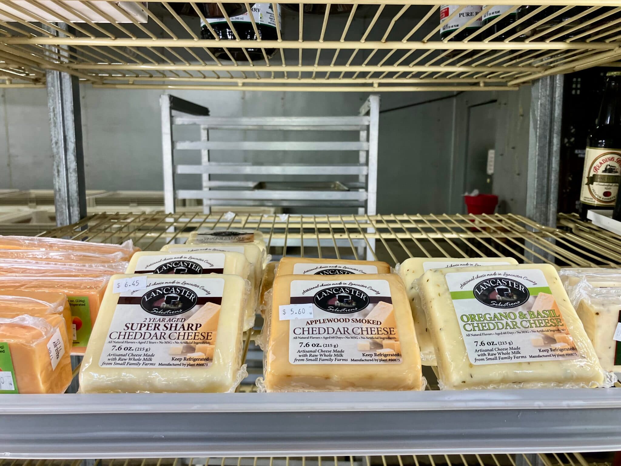 A display of various cheddar cheeses in a refrigerated case, labeled with prices and flavors.