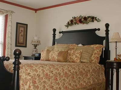 A cozy bedroom featuring a black wooden bed with decorative floral bedding and a lamp beside it.