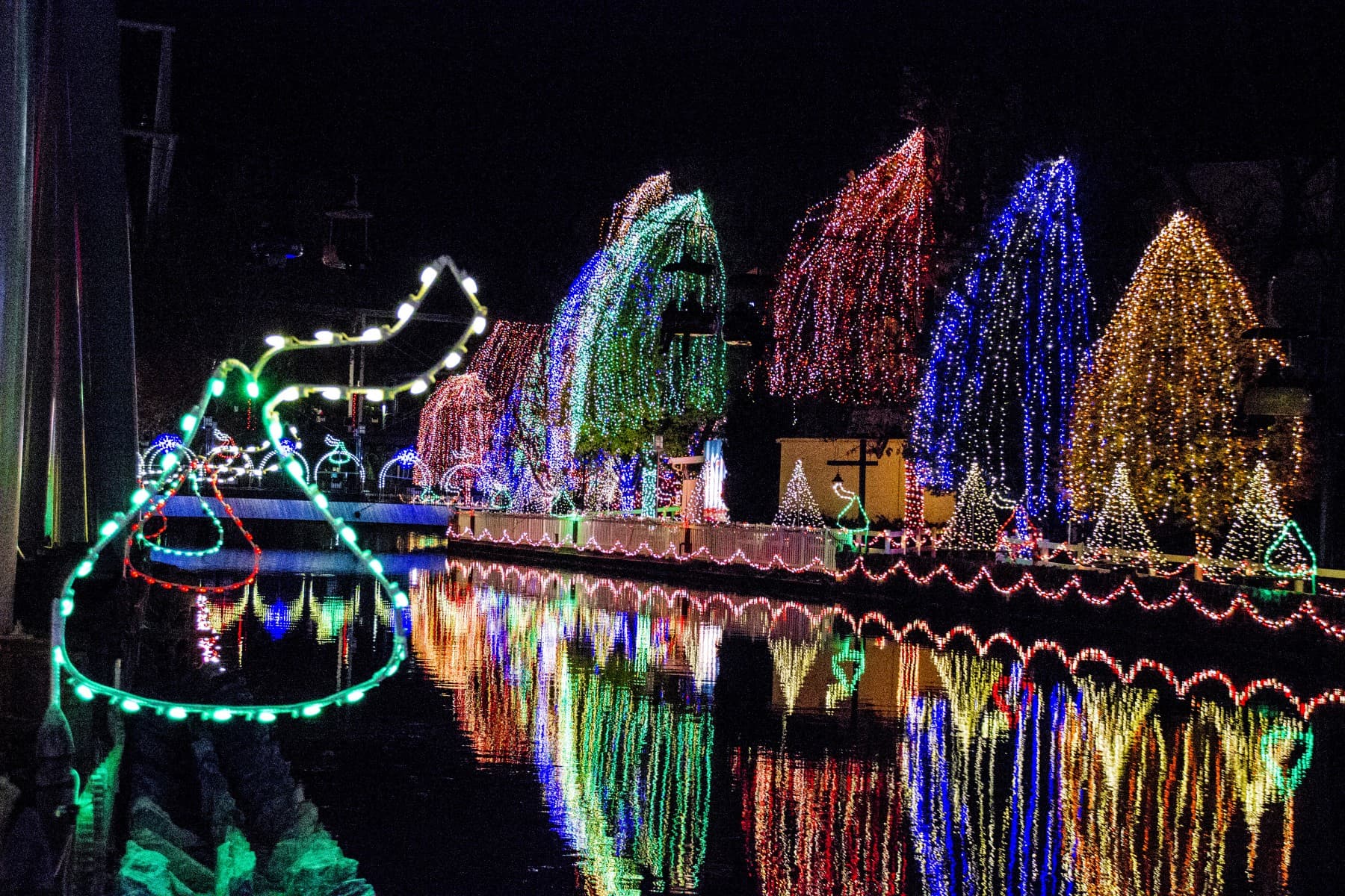 A canal lined with colorful holiday lights reflecting on the water at night.