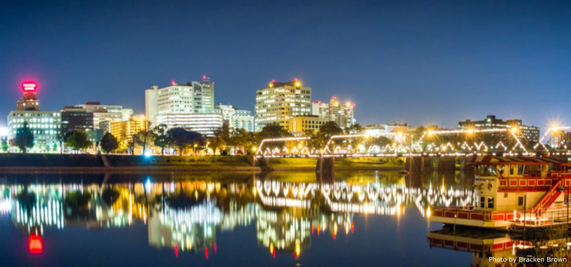 City skyline at night reflected in a river with lights along the waterfront.