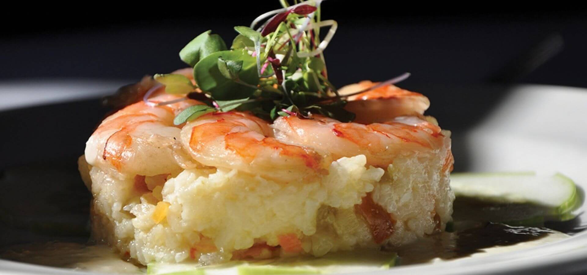 A plated dish of shrimp atop creamy polenta garnished with microgreens.