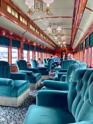 Interior of a vintage train car with green velvet seating and large windows, occupied by several passengers.
