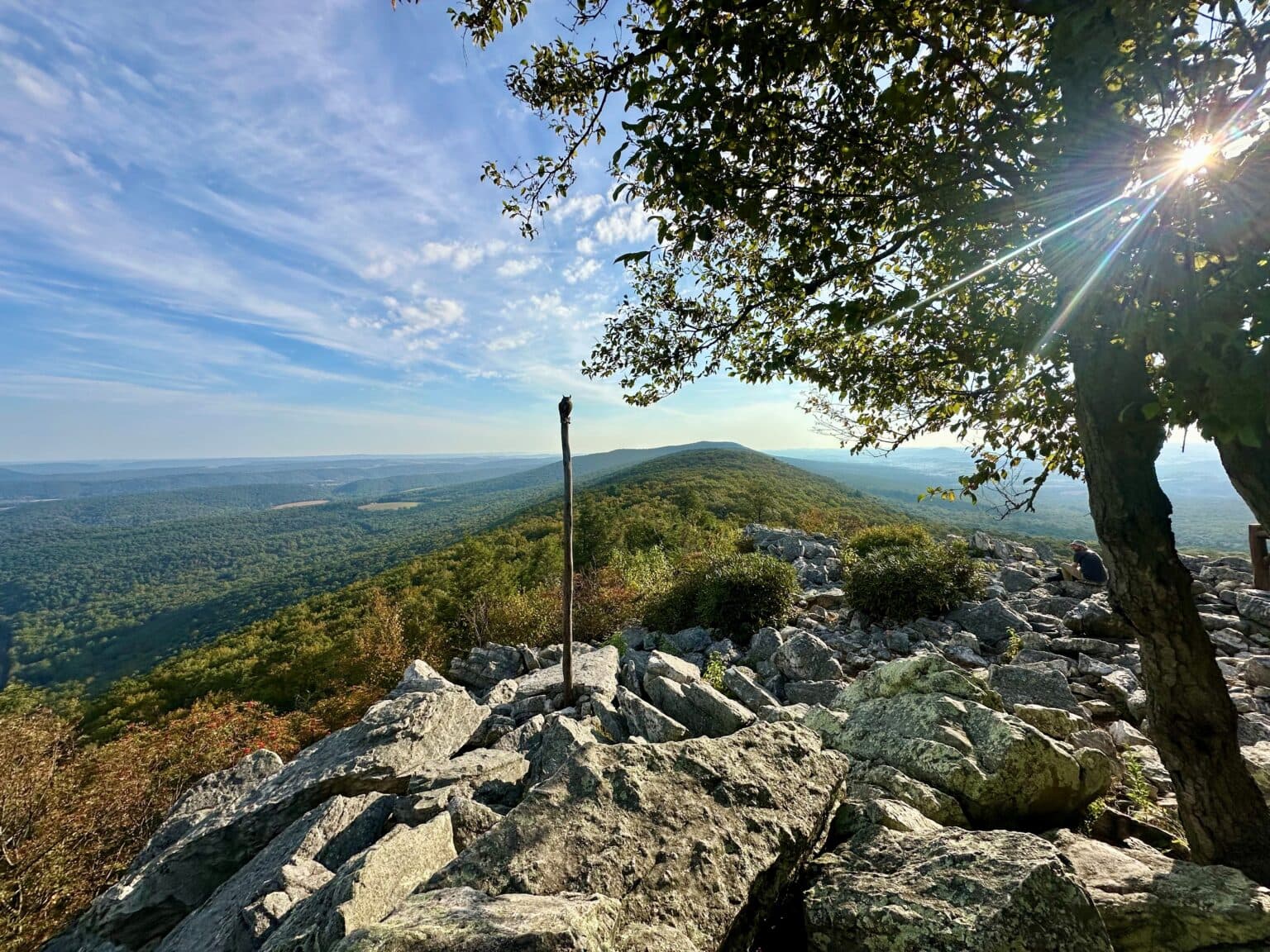 A panoramic view from a rocky mountain top overlooking lush green valleys and distant hills under a clear sky.