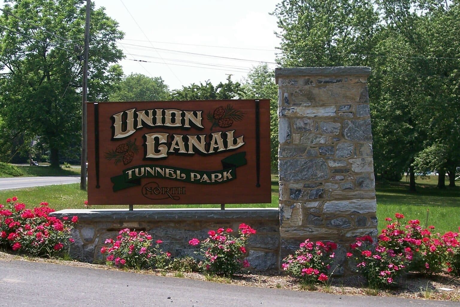 Sign marking the entrance to Union Canal Tunnel Park, surrounded by greenery and flowers.