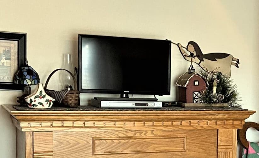 A wooden mantel displays a television, decorative items, and a small barn figurine.