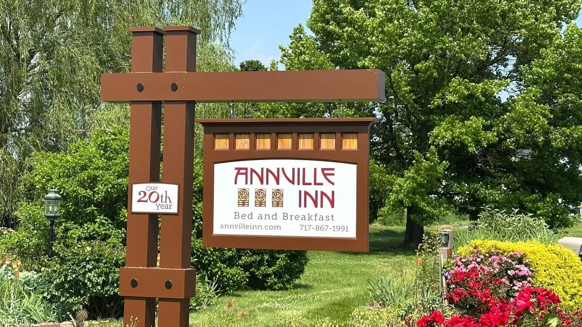 Sign for Annville Inn Bed and Breakfast, celebrating 20 years, with lush greenery and flowers surrounding it.