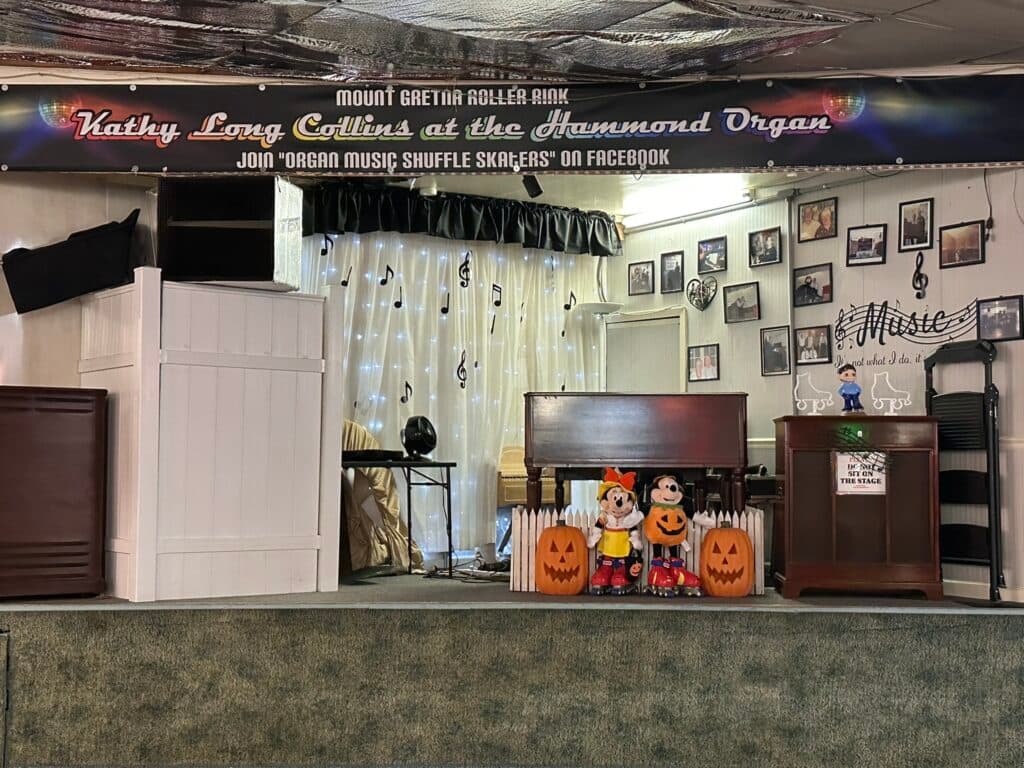 A stage decorated with a banner for a performance featuring Kathy Long Collins at the Hammond Organ, with a backdrop of musical notes and festive pumpkin decorations.