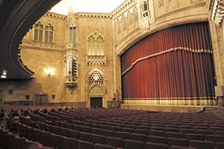 An empty vintage theater interior with ornate architecture and a red stage curtain.