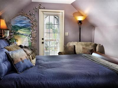 A cozy bedroom with a blue-themed bed, decorative pillows, and a door leading to a balcony.