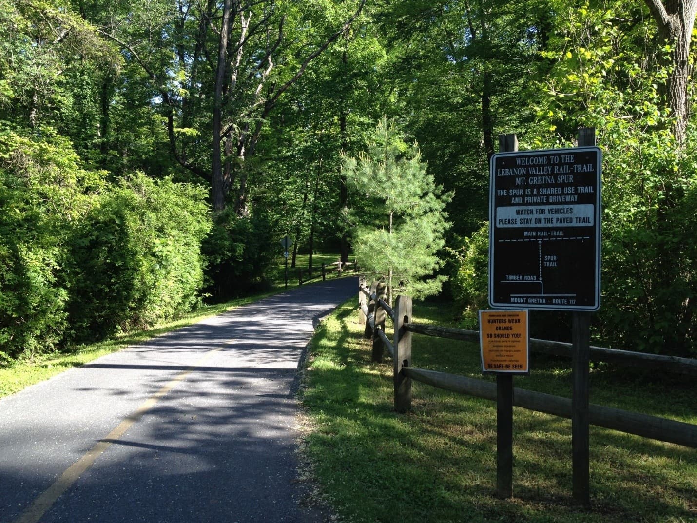 A paved trail surrounded by greenery with a sign welcoming visitors to the Lebanon Valley Rail Trail.