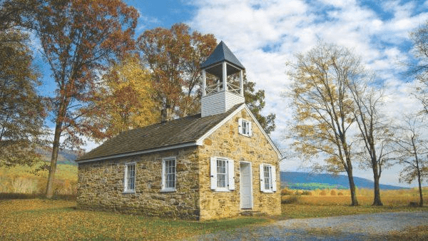 A quaint stone building with a bell tower surrounded by autumn trees.