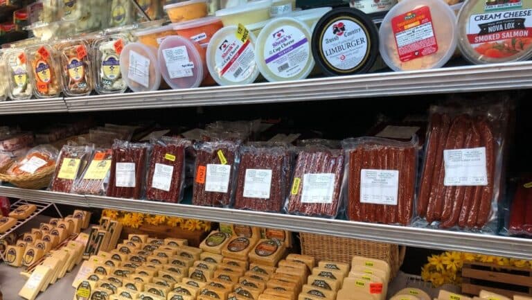 A variety of packaged meats and cheeses displayed in a refrigerated case at a market.