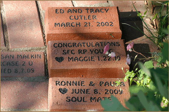 A collection of engraved bricks commemorating names and dates in a garden pathway.