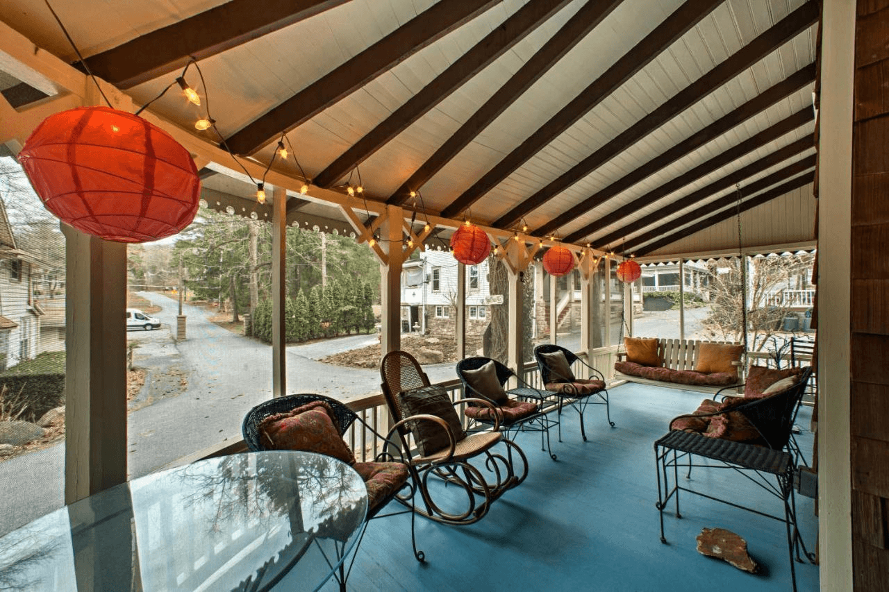 A cozy porch with string lights and red lanterns, furnished with a glass table and various seating options, overlooking a quiet street.