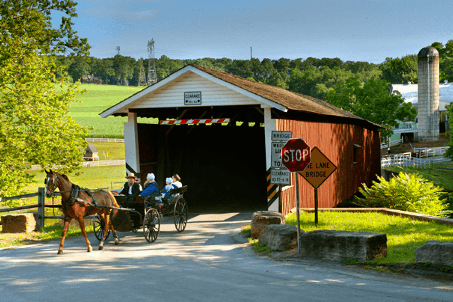 A horse-drawn carriage approaches a covered bridge in a rural landscape.