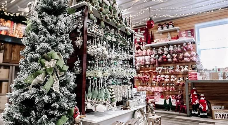A beautifully decorated Christmas display featuring a frosted tree and various ornaments in a festive shop.