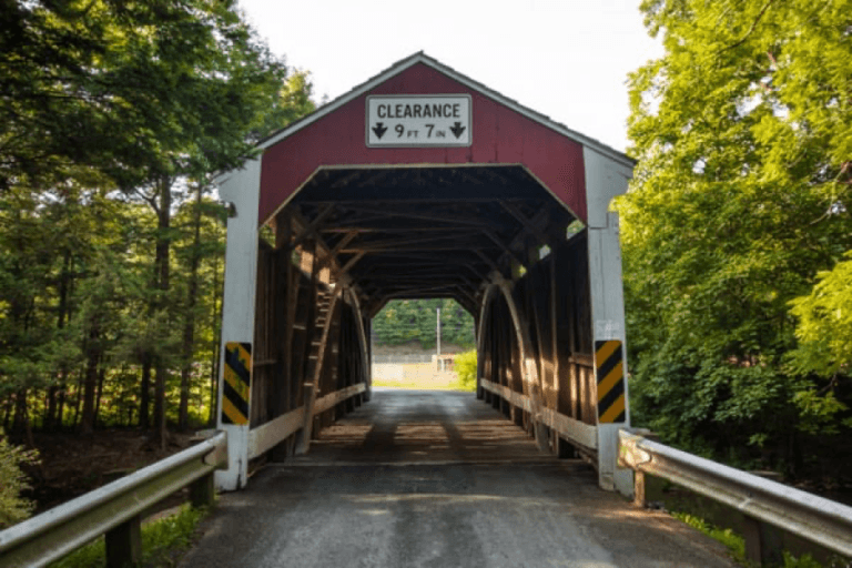 A view of a covered bridge surrounded by trees, with a clearance sign indicating 9 feet 7 inches.