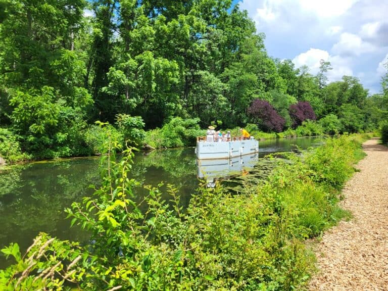 A boat floats on a calm canal surrounded by lush green trees.