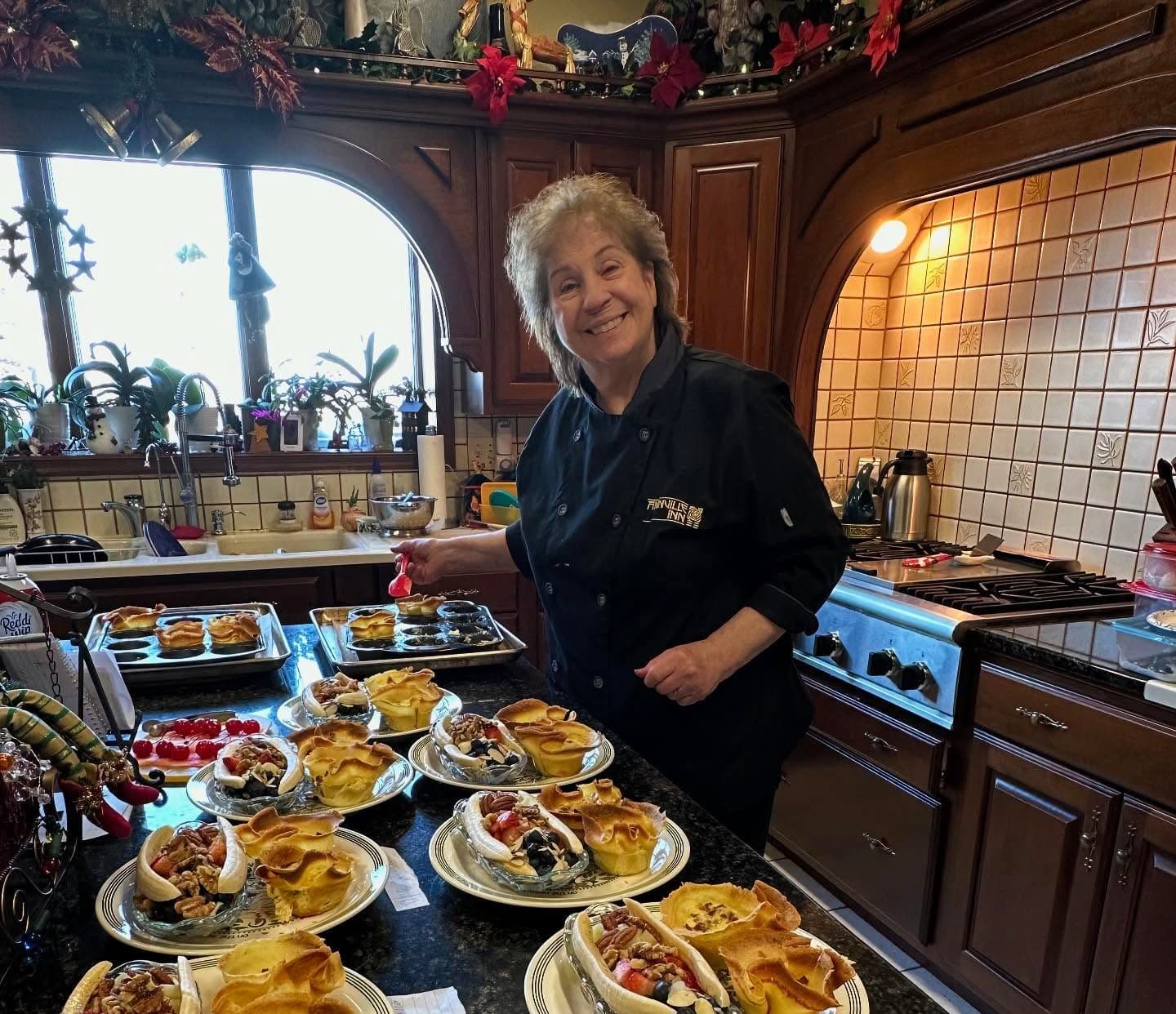 A smiling woman in a chef's jacket prepares colorful dishes in a festive kitchen.