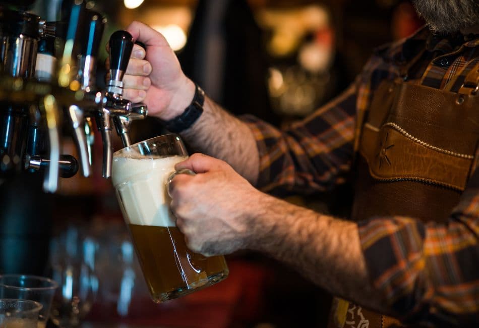 A bartender pours a frothy beer from a tap into a glass.