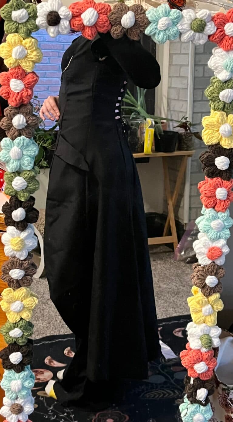A person in a black dress stands in front of a floral mirror frame.