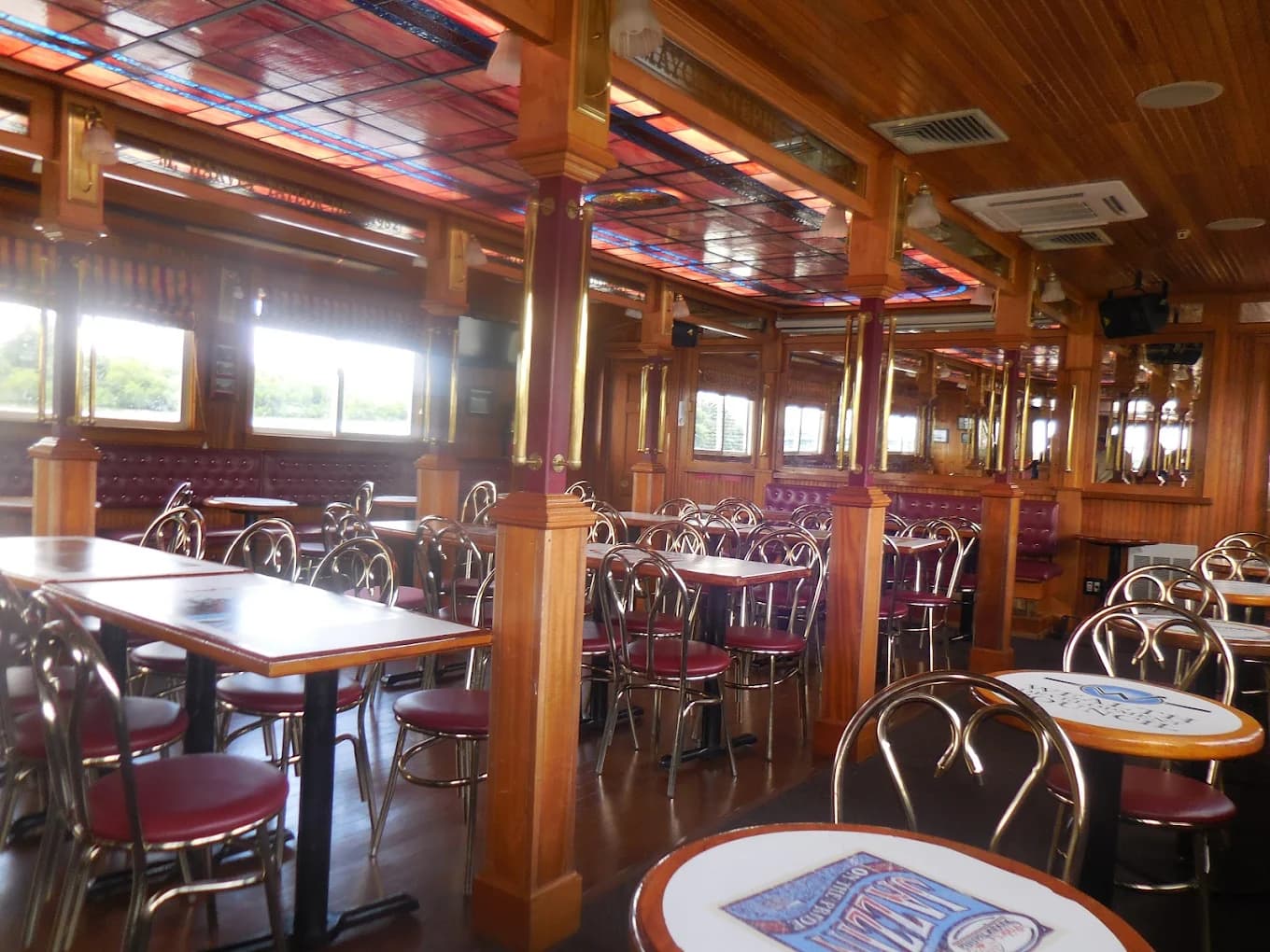 Interior of a dining area with wooden decor, empty tables, and windows showing outdoor views.