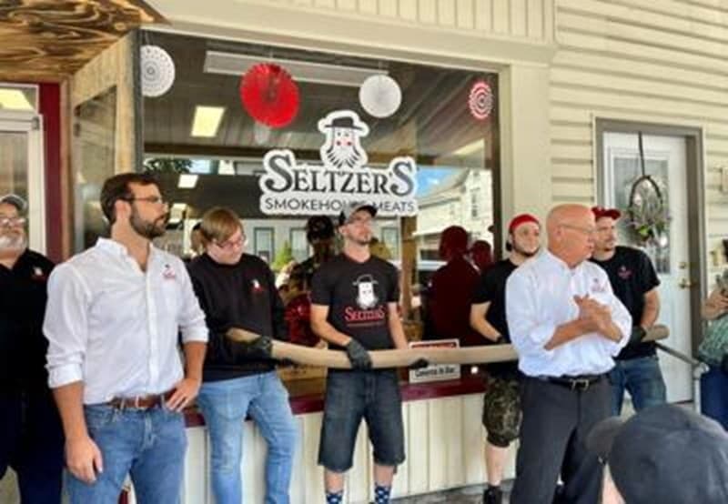 A group of people stands outside Seltzer's Smokehouse Meats during a formal event or gathering.