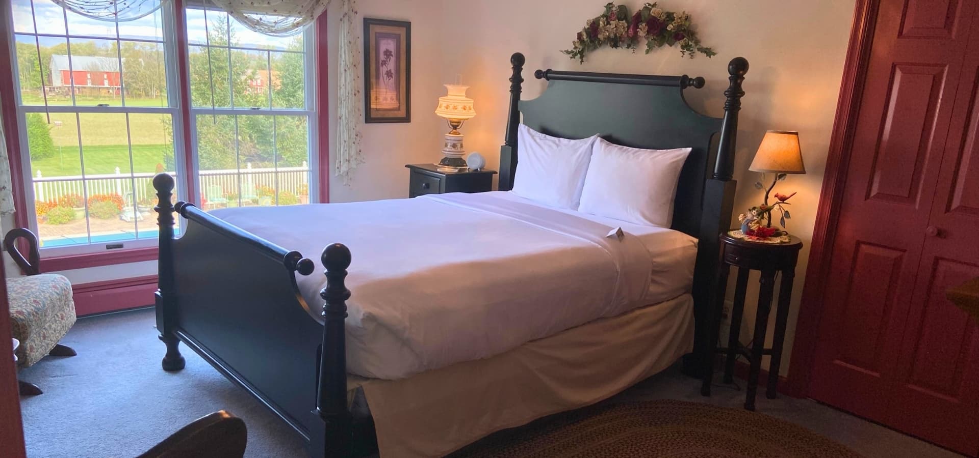 A cozy bedroom featuring a black four-poster bed, a small bedside table with a lamp, and a bright window view.