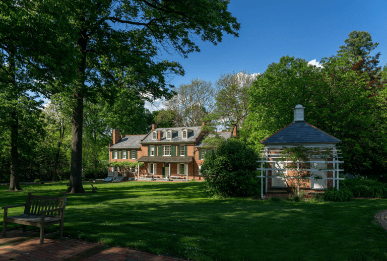 A brick house surrounded by lush greenery and a gazebo in a sunny yard.