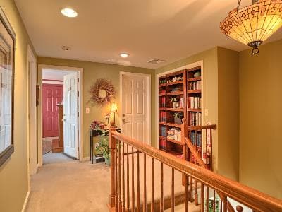A well-lit hallway with a wooden railing, bookshelves, and doorways leading to adjacent rooms.