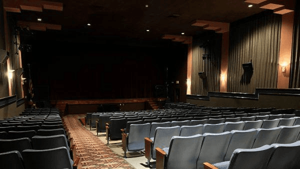 Interior of a small theater with empty blue seats and a dark stage.