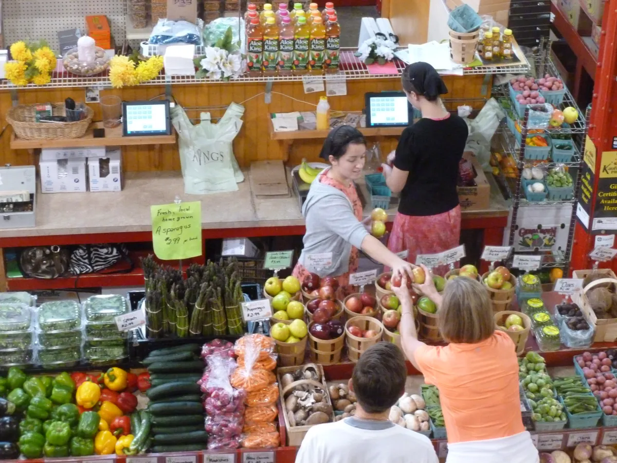 A bustling market stall with customers interacting while surrounded by a variety of fresh produce.