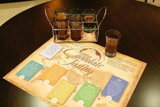 A tray with several shot glasses of chocolate drinks sits atop a colorful tasting guide on a table.