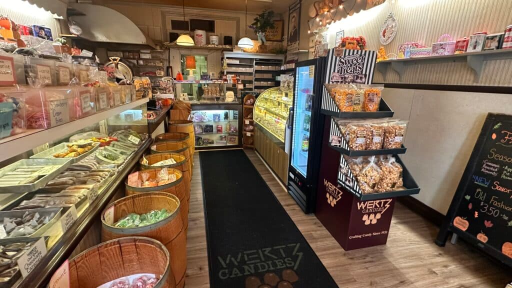 A cozy candy shop interior featuring colorful bins of sweets, a display case, and shelves of treats.
