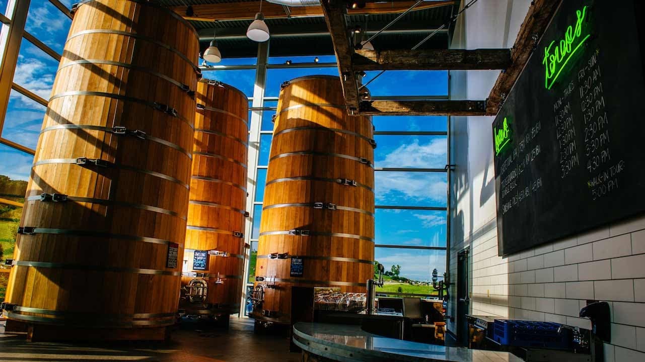 Interior of a bright space featuring large wooden fermentation barrels and a chalkboard menu.