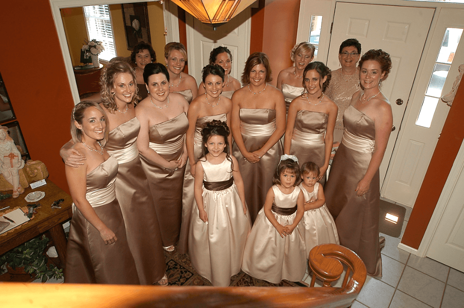 A group of women in matching brown and beige dresses poses together at a home, smiling and celebrating.