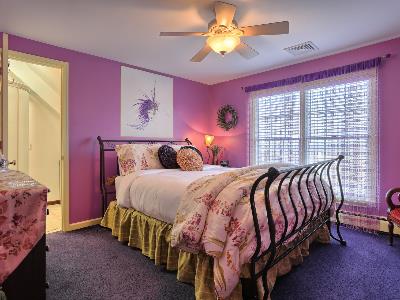 A cozy bedroom with a pink color scheme, featuring a black metal bed, floral bedding, and large windows.