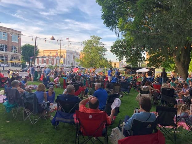A large crowd of people gathers in a park, enjoying an outdoor event under a warm sky.